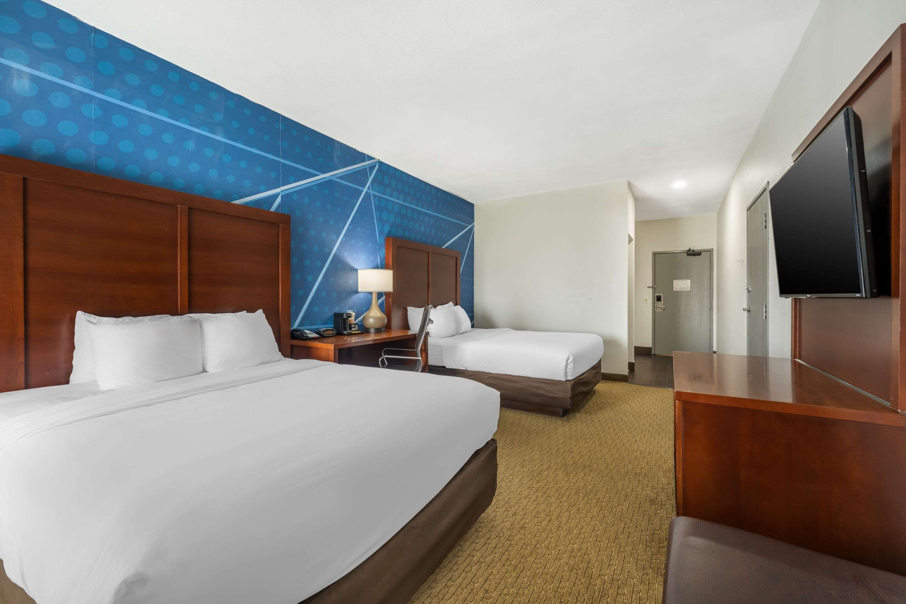 Une chambre d’hôtel avec deux lits, un bureau, une chaise, une télévision et une porte de salle de bain.
