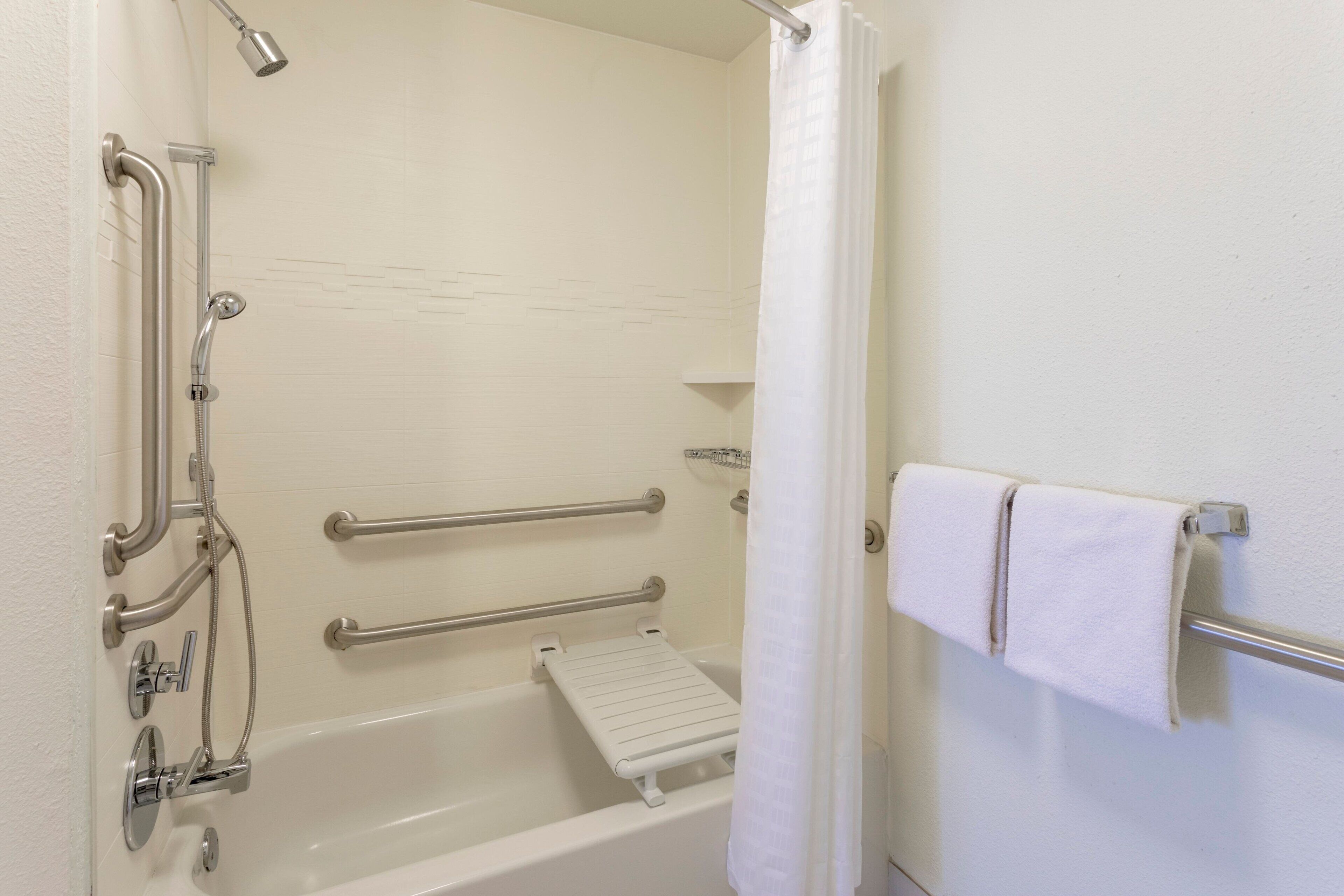 Un baño con bañera, barras de apoyo, ducha y perchero para toallas.