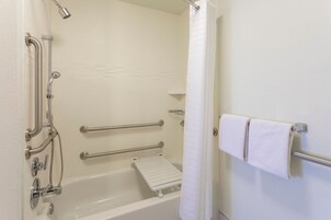 Un baño con bañera, barras de apoyo, ducha y perchero para toallas.