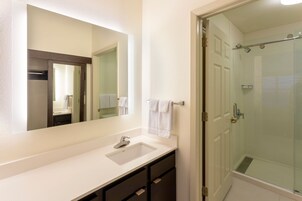 Un baño con lavamanos blanco, un espejo grande y una cabina de ducha de vidrio.