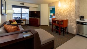 A hotel room with a sofa, a small dining table, a TV, a kitchen area, and a view of the outdoors. - Residence Inn by Marriott Minneapolis St. Paul/Roseville (Roseville)
