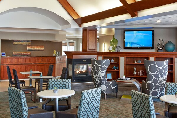 A hotel lobby with a fireplace, seating area, television, and wooden paneling. - Residence Inn by Marriott Minneapolis St. Paul/Roseville (Roseville)