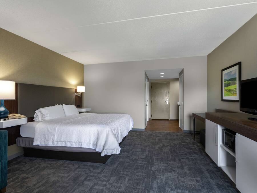 Ein Hotelzimmer mit Bett, Nachttisch, Lampe, Fernseher und Schreibtisch mit Mikrowelle.