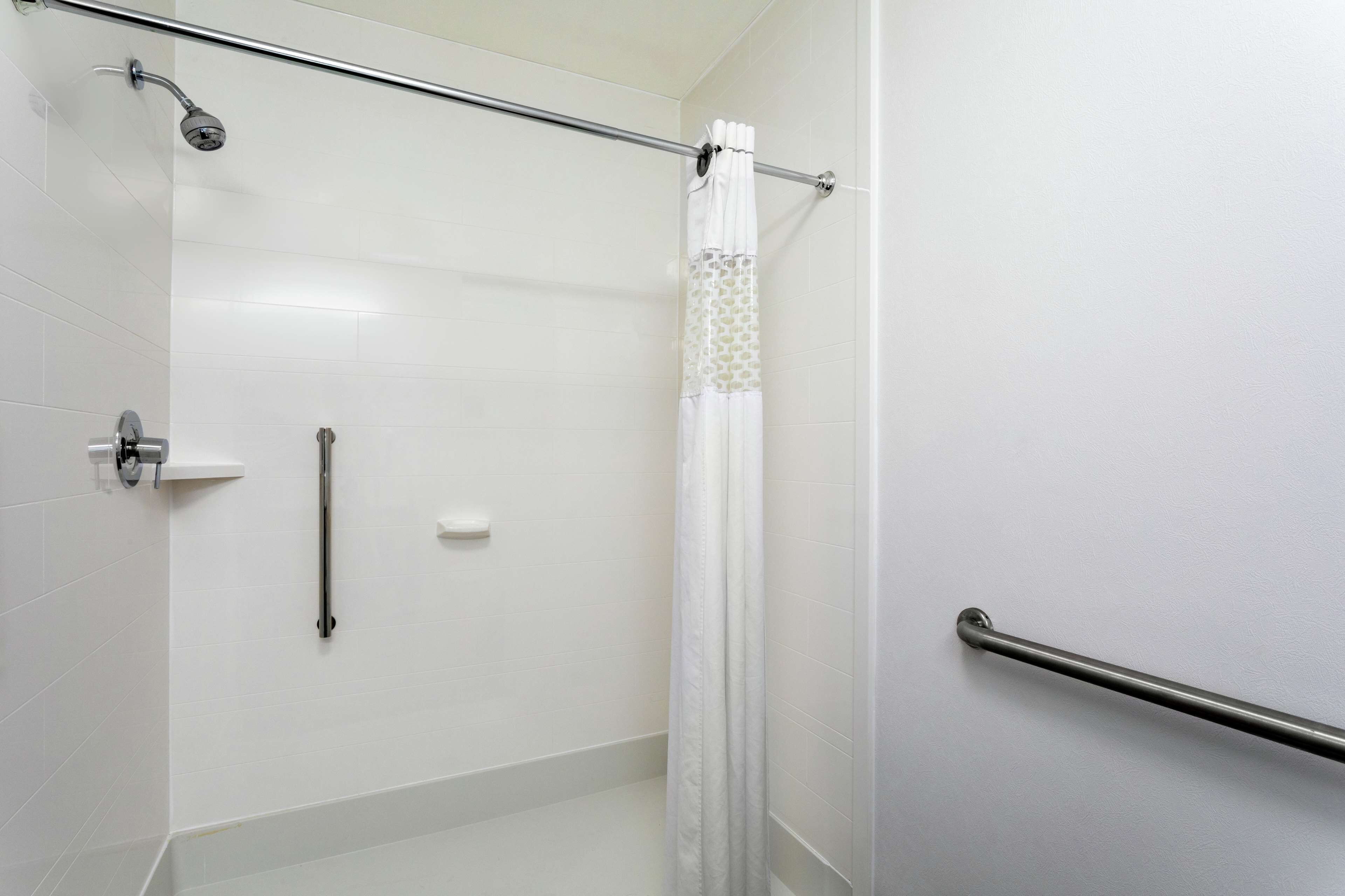 A modern bathroom with white tiles, a shower with a glass door, a toilet paper holder, and a grab bar.
