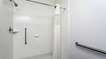 A modern bathroom with white tiles, a shower with a glass door, a toilet paper holder, and a grab bar.