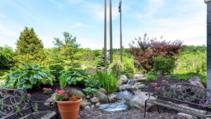 Ein Garten mit einer Bank, einem kleinen Bach und einem Fahnenmast.