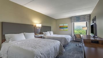 A hotel room with two beds, a desk, a chair, a TV, and a window with a view of the outdoors.