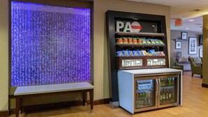 Ausstellung von PA Treats mit Snacks und Getränken, eine Bank und eine Wand mit blauer Lichtinstallation.