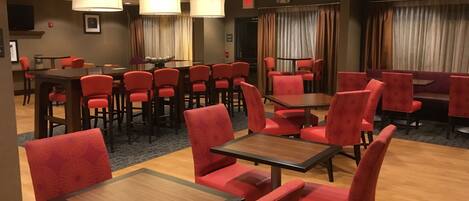 A hotel dining area with red upholstered chairs and tables, a large dining table, and pendant lighting.