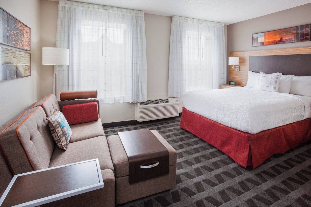 A hotel room with a bed, a sofa, a side table, and a lamp.