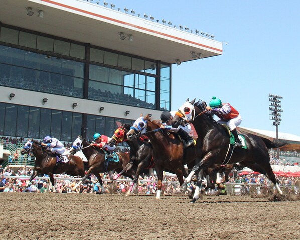 Una carrera de caballos con jinetes, una multitud de espectadores y un edificio grande al fondo.