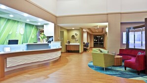 A reception area with a curved counter, a seating area with a red sofa and a yellow armchair, and a wooden floor. - SpringHill Suites by Marriott Chicago Naperville/Warrenville (Warrenville)