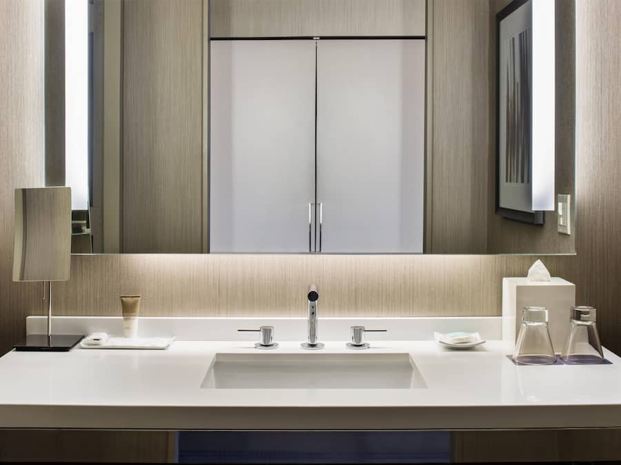 A modern bathroom with a large mirror, a sink with two faucets, and a towel dispenser.