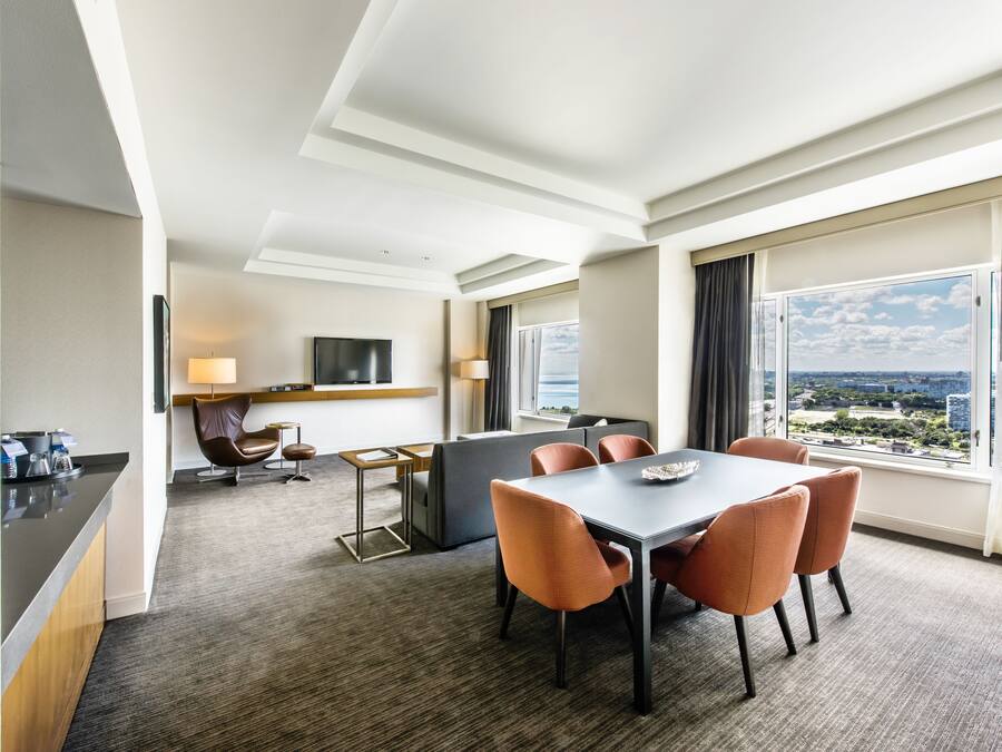 A hotel room with a dining area, a sofa, a TV, and a view of the city.