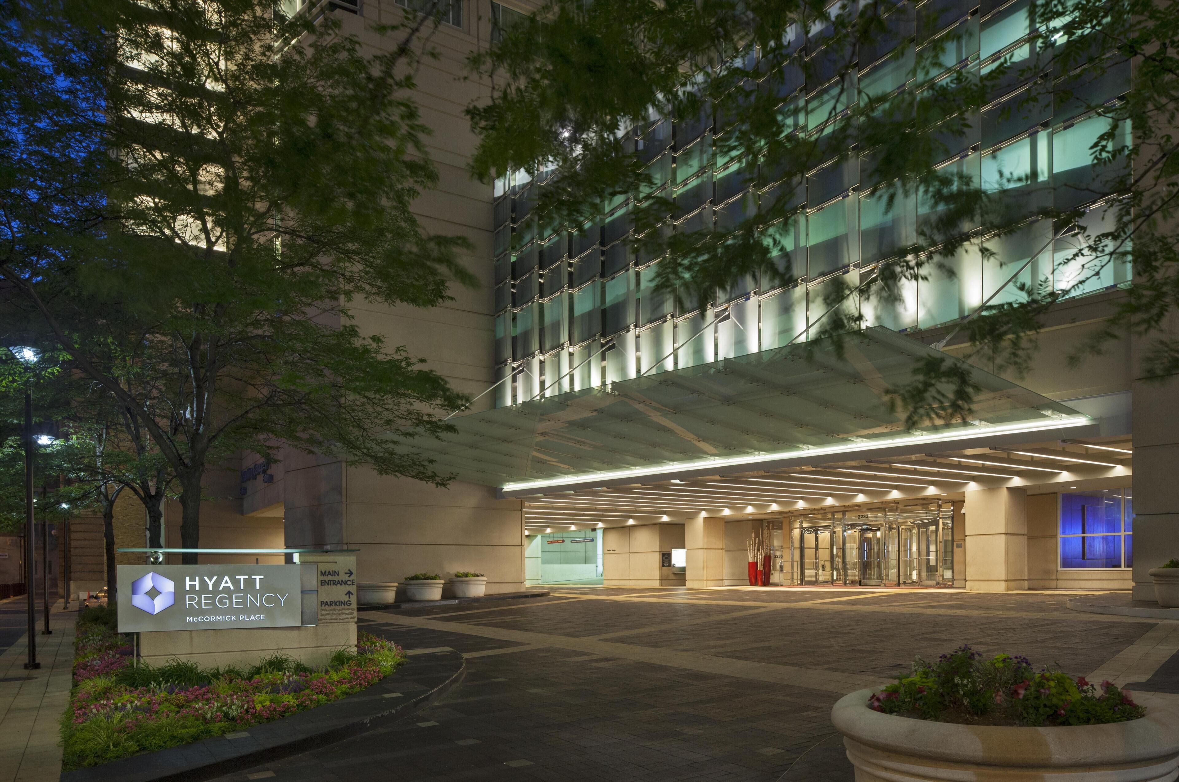 A Hyatt Regency McCormick Place hotel entrance with a glass facade, a covered entrance area, and a sign indicating the main entrance and parking.