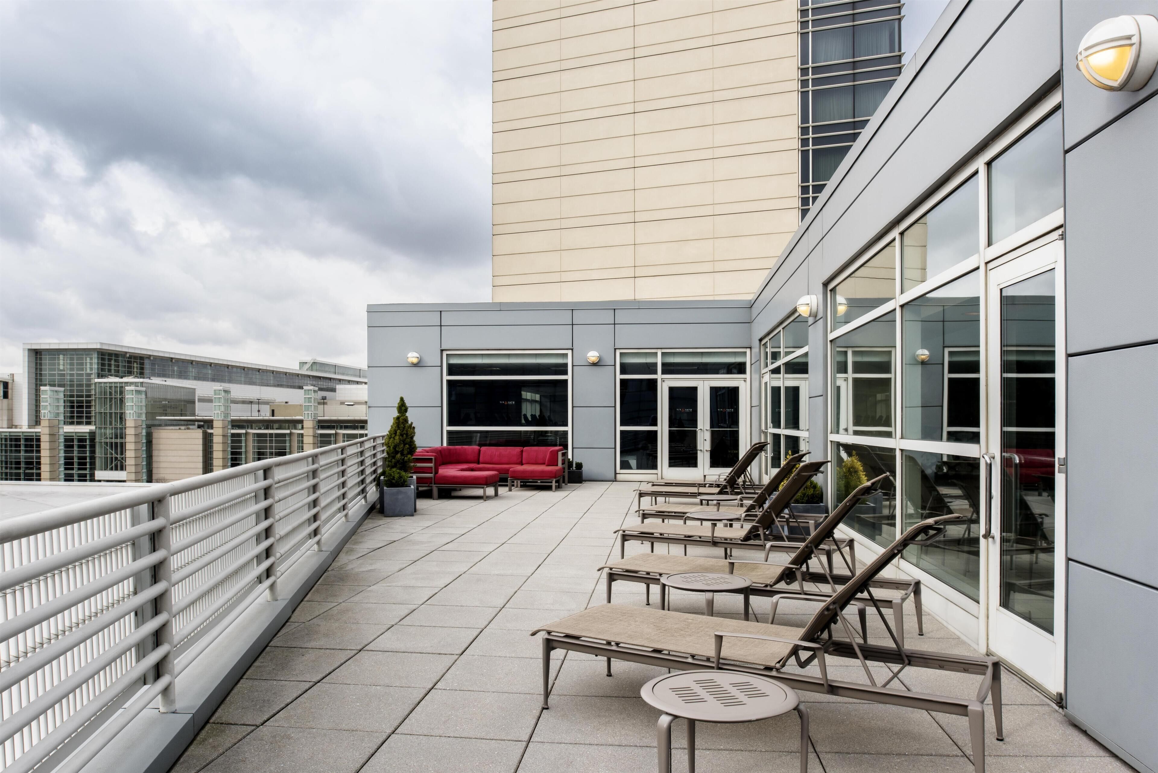 A rooftop terrace with outdoor seating, a red sofa, and a tall building in the background.