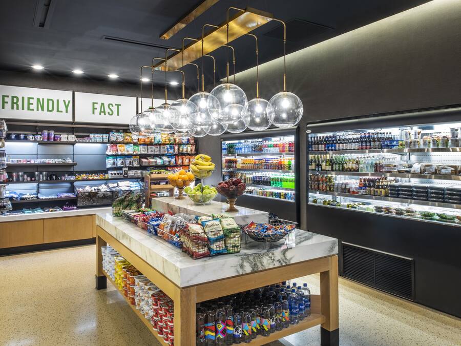 A grocery store interior with a marble counter, shelves stocked with snacks, and a refrigerated section.