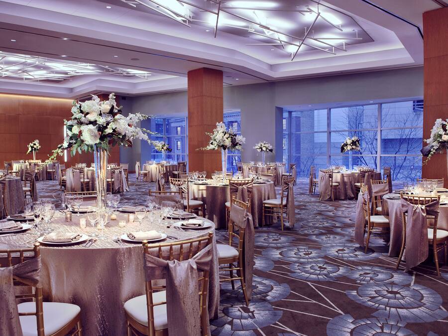 Une salle de banquet avec des tables rondes, des chaises et des centres de table floraux.
