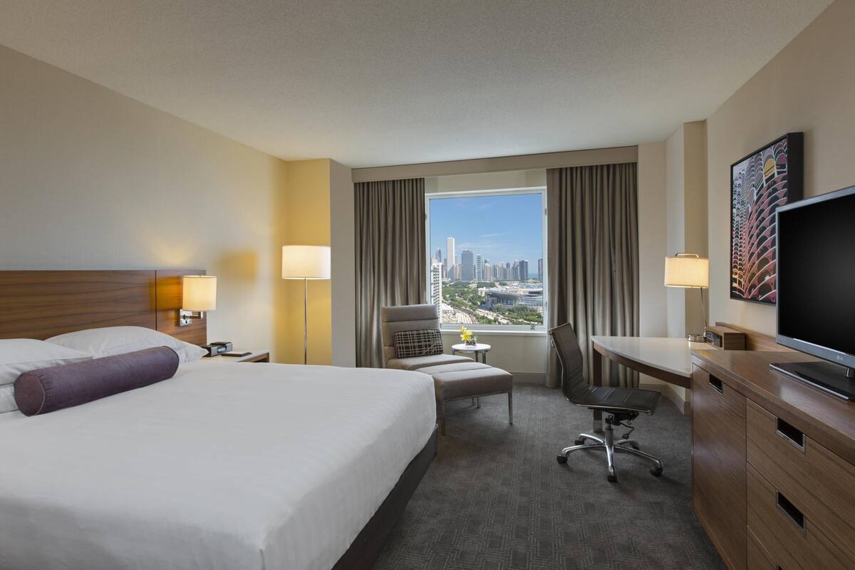Quarto de hotel com cama grande, escrivaninha, cadeira, televisão e vista para a cidade.