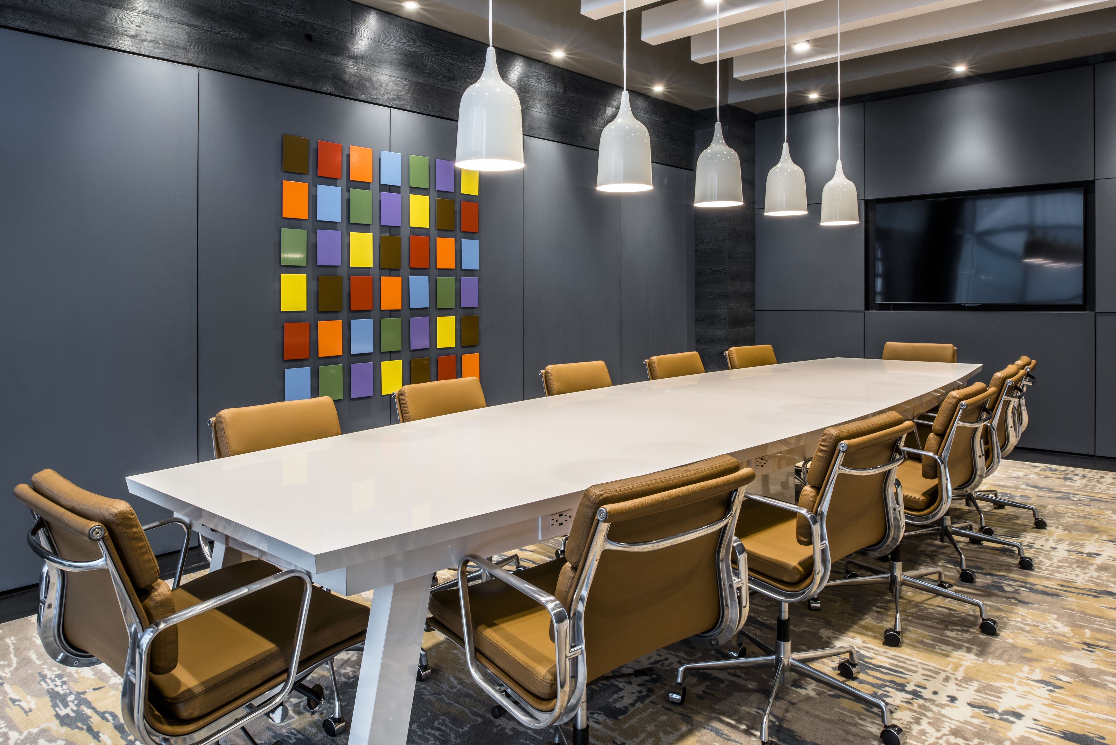 A conference room with a long table, brown leather chairs, white pendant lights, and a colorful wall art piece.