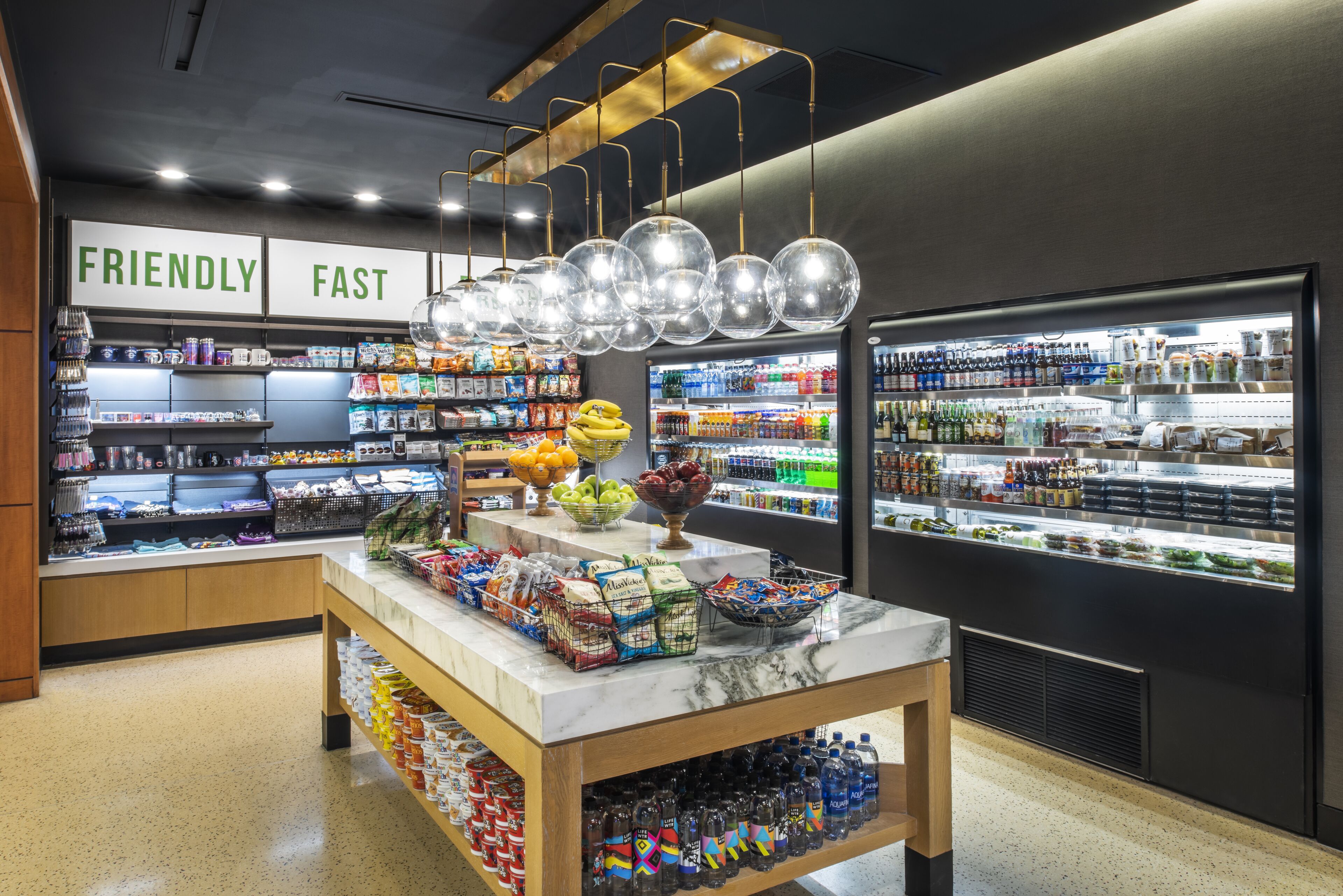 A grocery store interior with a marble counter, shelves stocked with snacks, and a refrigerated section.