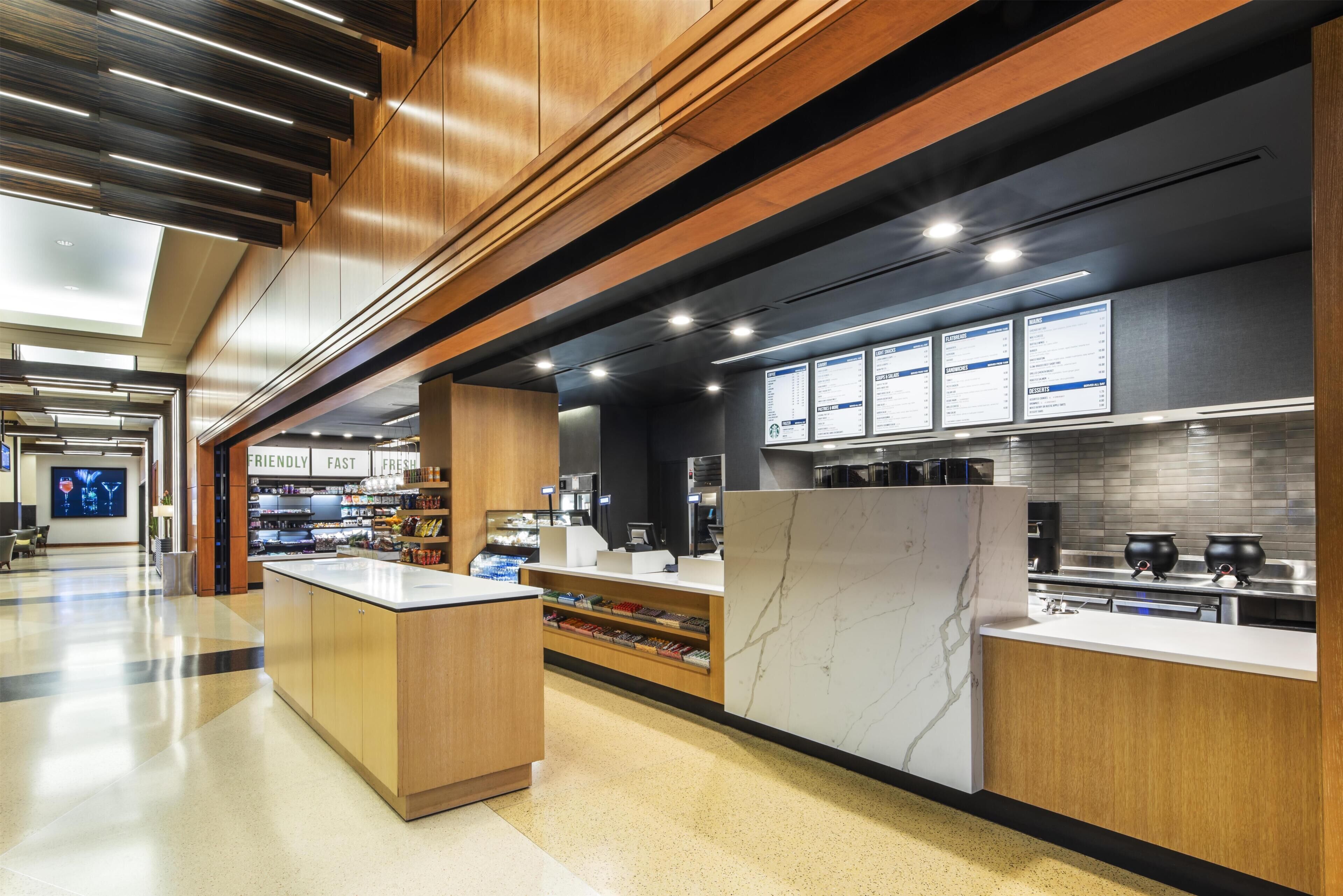 A modern kitchen area with wooden cabinetry, marble countertops, and overhead lighting.