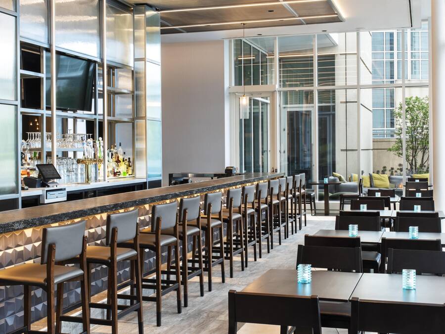 A modern bar area with a long counter, multiple bar stools, and a seating area with tables and chairs.
