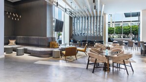 A modern hotel lobby with a sectional sofa, round tables, and chairs, a flat-screen TV, and large windows offering city views. - Hyatt Regency McCormick Place Chicago    (Chicago)