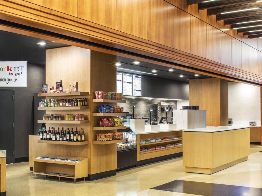 A modern market area with wooden counters, shelves stocked with various products, and a sign indicating order pick-up.