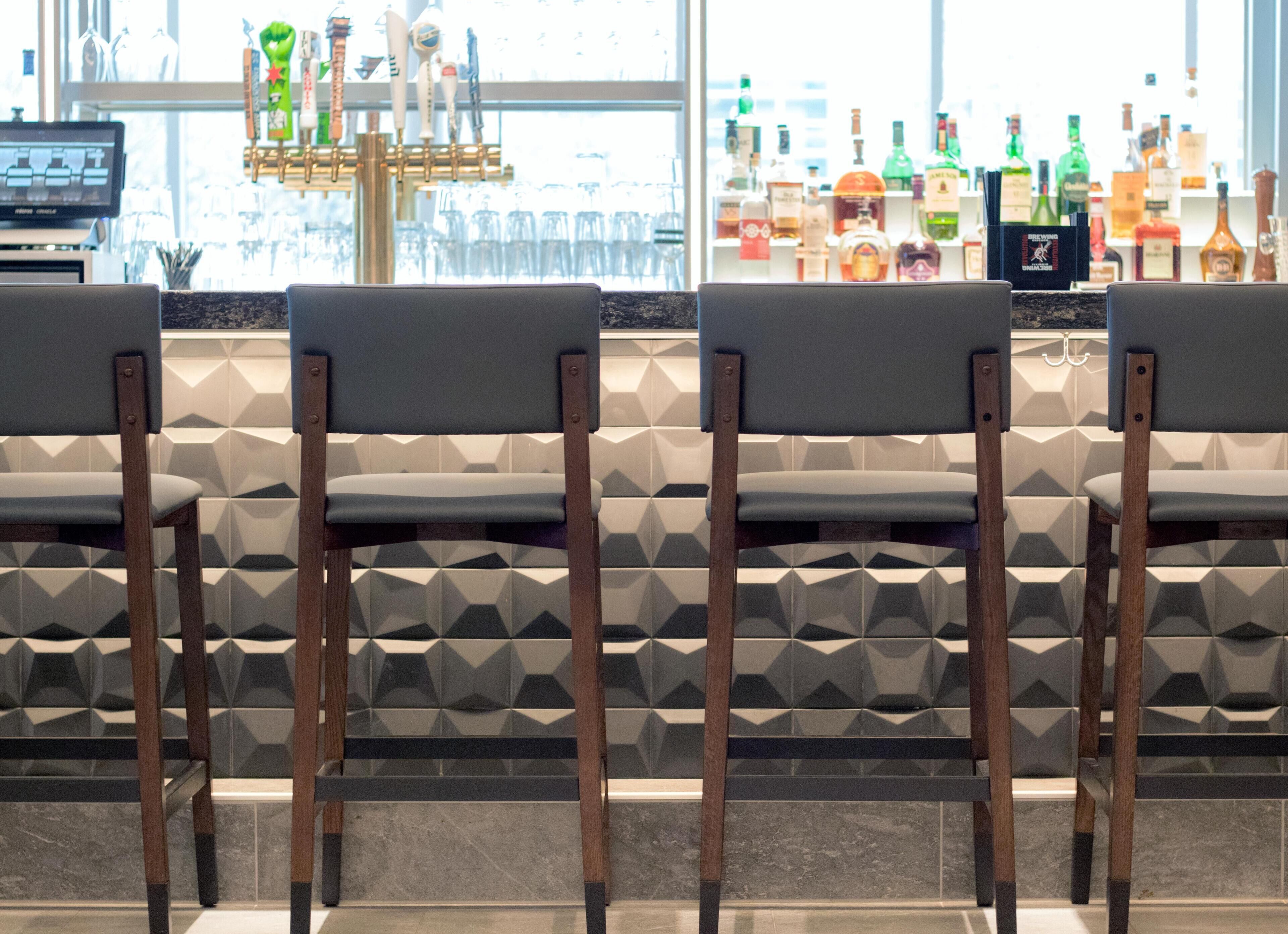 A bar area with four chairs, a bar counter, and a variety of liquor bottles.