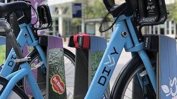 Un vélo bleu orné d’autocollants « GO WITH BLUE » et « FRESH », garé à côté d’un support à vélos violet et vert.