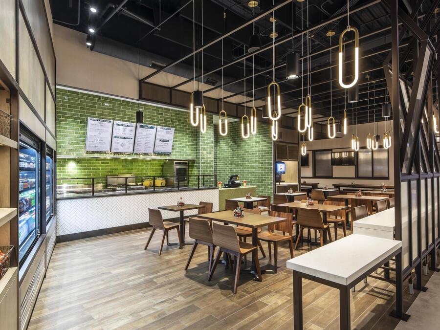 A restaurant with a green brick wall, hanging pendant lights, and wooden tables and chairs.