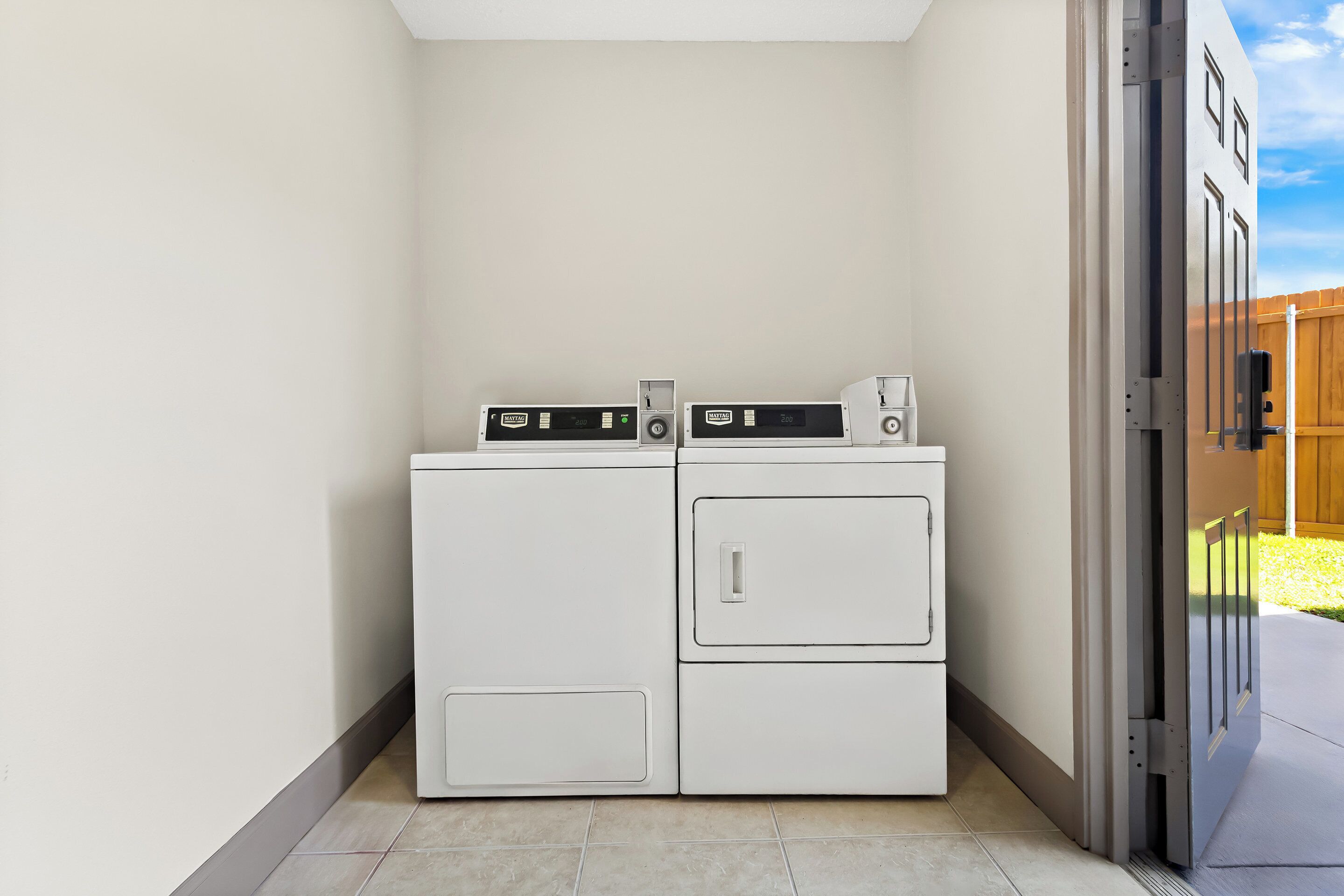 A laundry room with two stacked washers and dryers, a sliding door, and a wooden fence in the background.