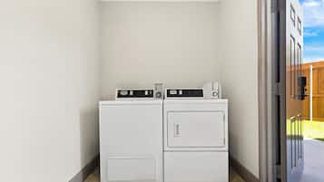 A laundry room with two stacked washers and dryers, a sliding door, and a wooden fence in the background.