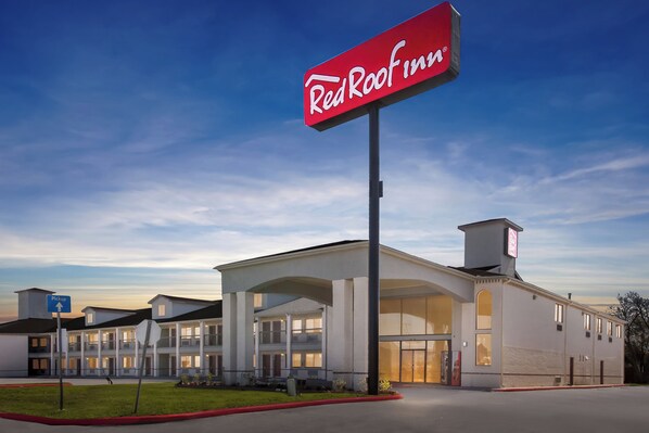 Un hôtel Red Roof Inn avec une grande enseigne, un parking couvert et une pelouse bien entretenue.