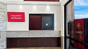 Ein Empfangsbereich mit einem Schild, das „Kostenloses WLAN in allen Zimmern“ ankündigt, einer modernen Tür und einer Coca-Cola-Werbung.