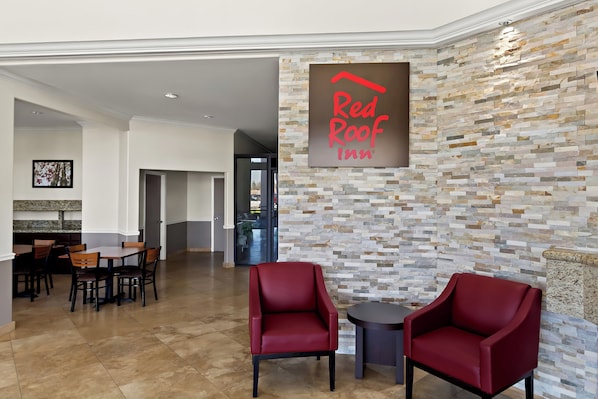 Un hall de Red Roof Inn con pared de piedra, dos sillones rojos y una zona de comedor con mesas y sillas de madera.