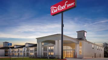 A Red Roof Inn with a large sign, a covered parking area, and a well-maintained lawn.