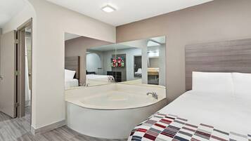 Quarto de hotel moderno com uma cama grande, uma banheira de hidromassagem no canto e um espelho grande que reflete o aposento.