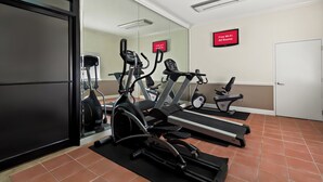 Ein Fitnessraum mit Laufbändern, Crosstrainern und einem Spiegel.