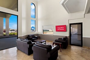 Un espace détente moderne avec des canapés en cuir, un téléviseur à écran plat et une grande fenêtre donnant sur le parking.
