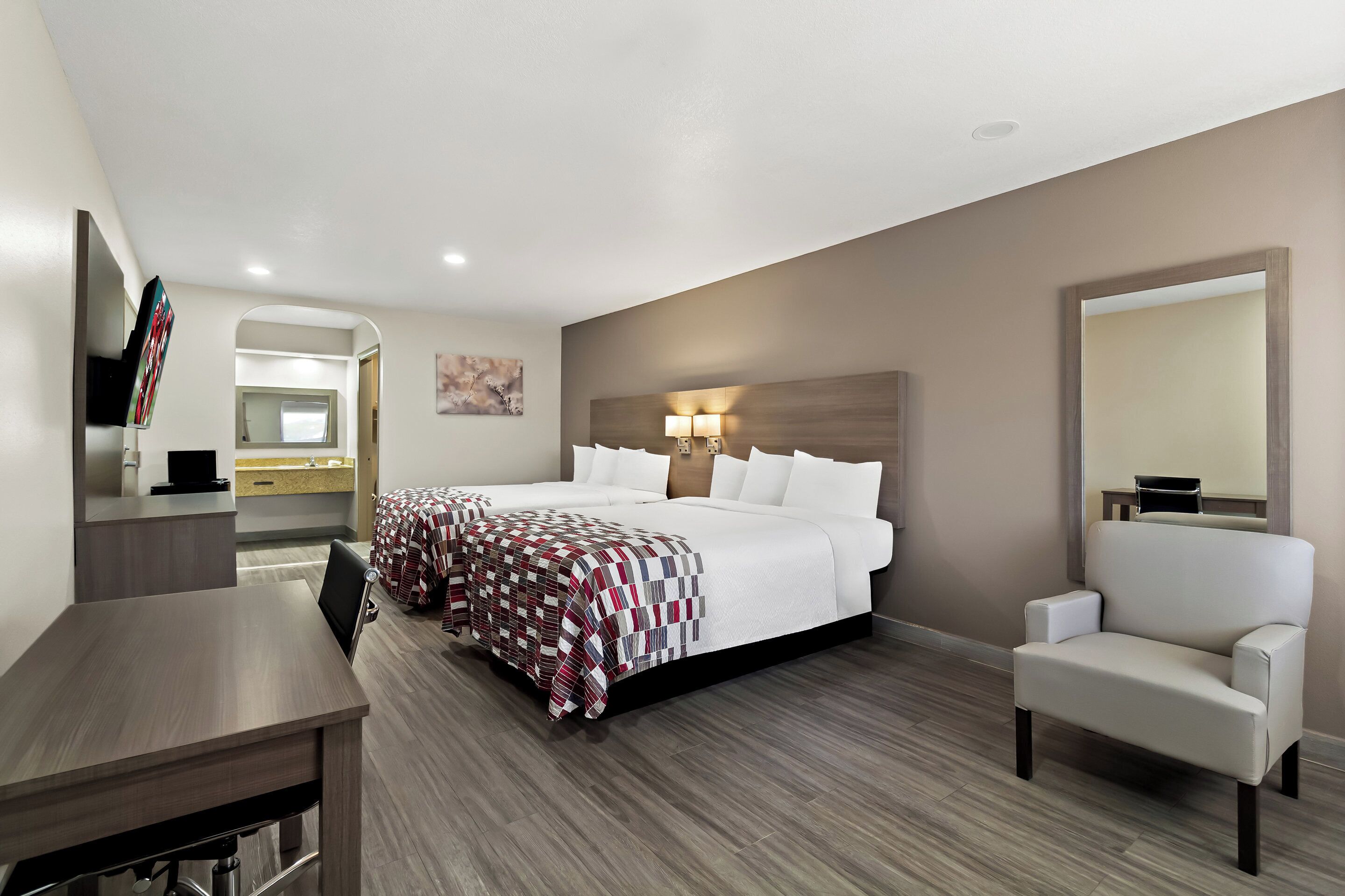 Una habitación de hotel con una cama grande, un escritorio, una silla y un espejo.