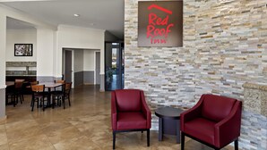 Un hall de Red Roof Inn con pared de piedra, dos sillones rojos y una zona de comedor con mesas y sillas de madera.