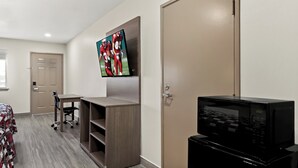 Habitación de hotel con televisor de pantalla plana en la pared, microondas en la encimera y escritorio con silla.