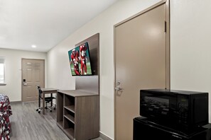 Une chambre d’hôtel équipée d’un téléviseur à écran plat fixé au mur, d’un four à micro-ondes posé sur le comptoir et d’un bureau avec une chaise.