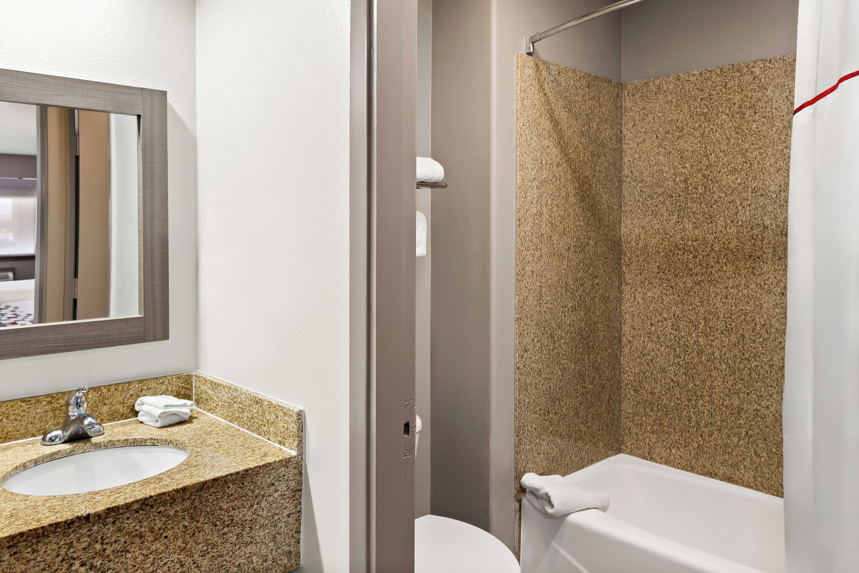 A bathroom with a granite countertop sink, a mirror, a toilet, and a shower with a textured wall.
