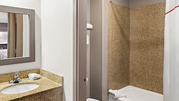A bathroom with a granite countertop sink, a mirror, a toilet, and a shower with a textured wall.