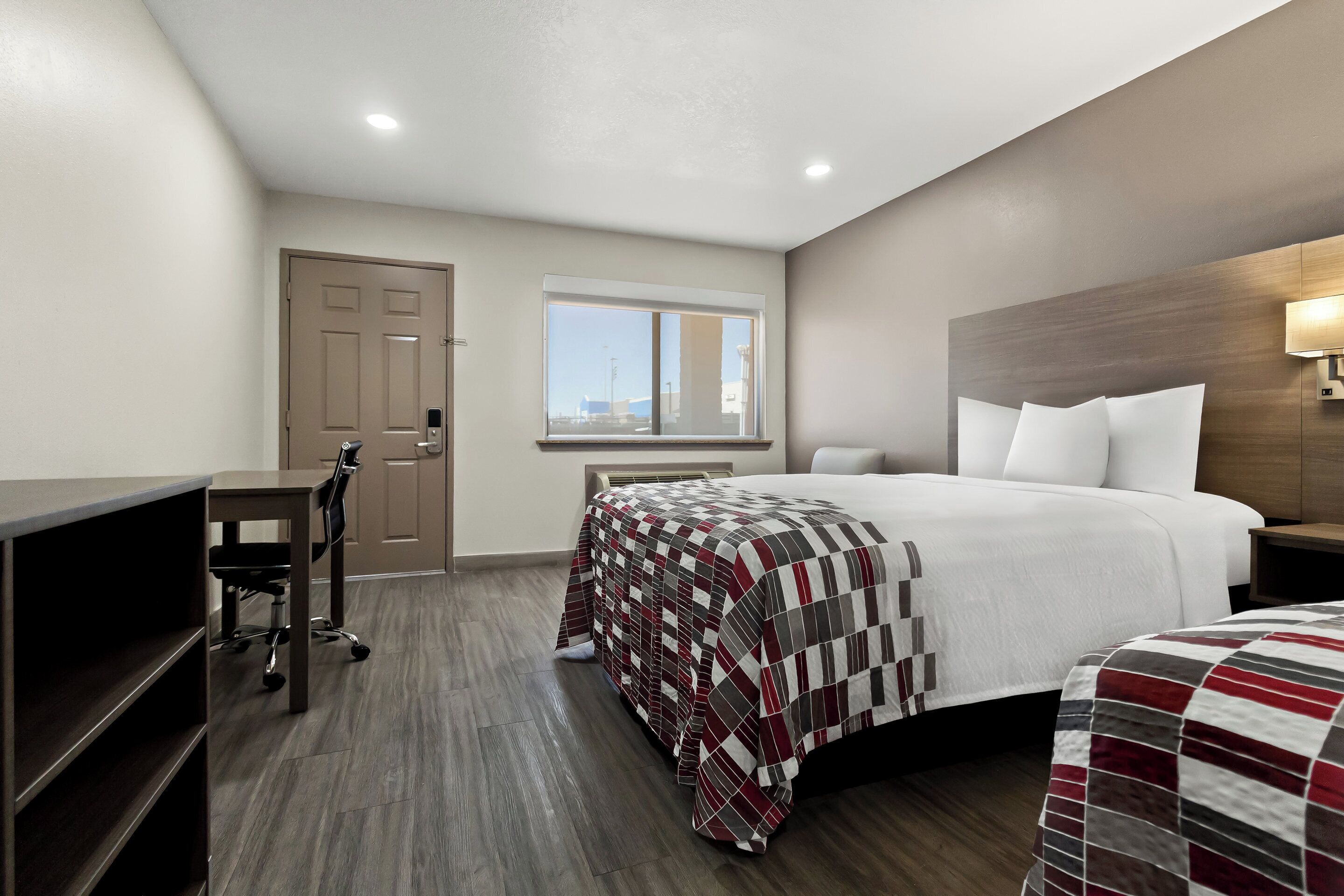Une chambre d’hôtel avec un lit, un bureau et une chaise. Il y a une fenêtre donnant sur l’extérieur.