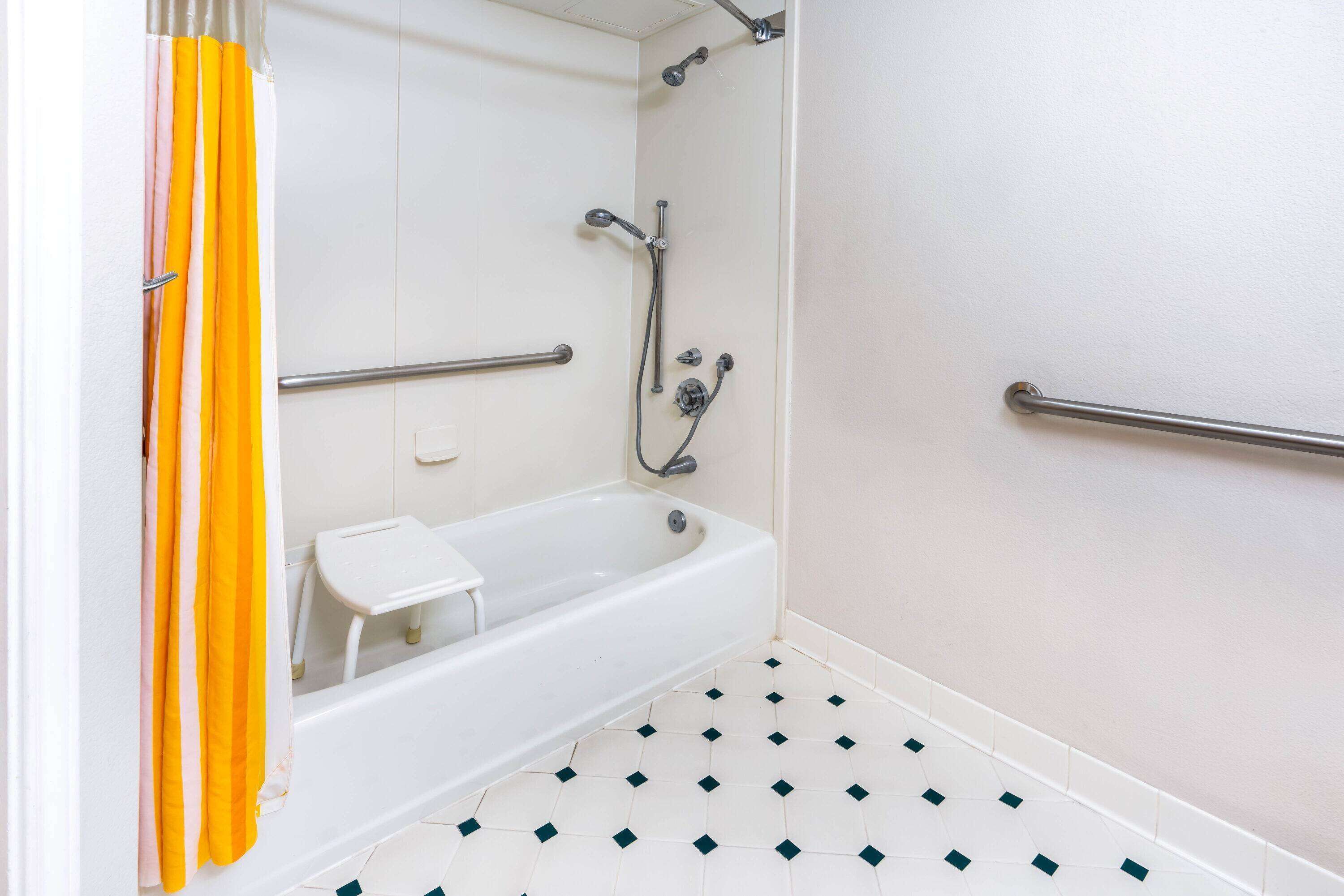 Une salle de bain avec une baignoire blanche, une pomme de douche et une barre d’appui.