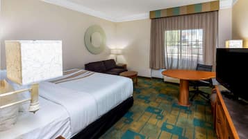 Habitación de hotel con cama, escritorio, silla, televisor y ventana con cortinas.